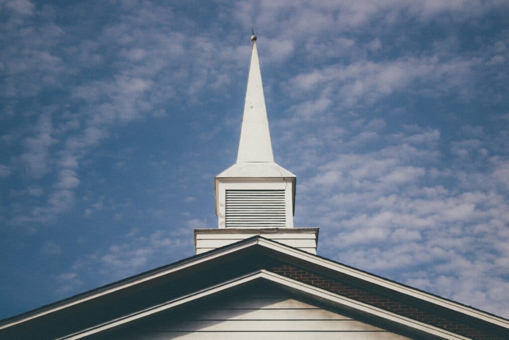 A church roof with a steeple. Blue sky with small white clouds in background.