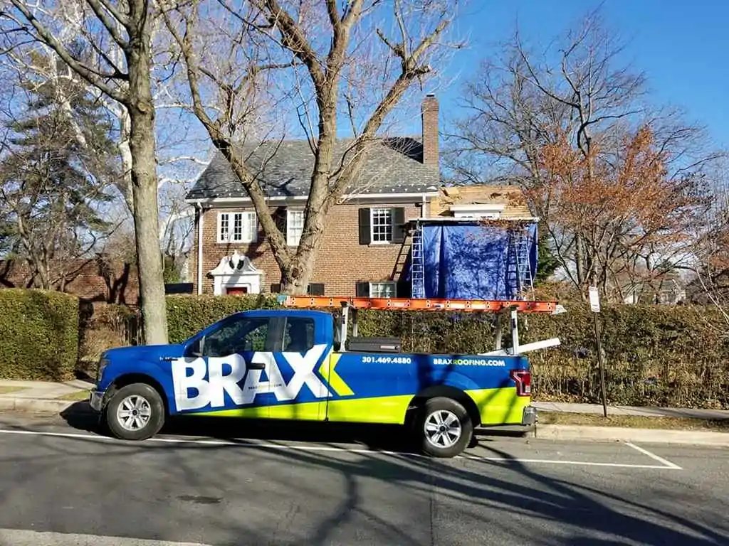 BRAX Roofing truck parked in front of a house with an emergency tarp on the roof.